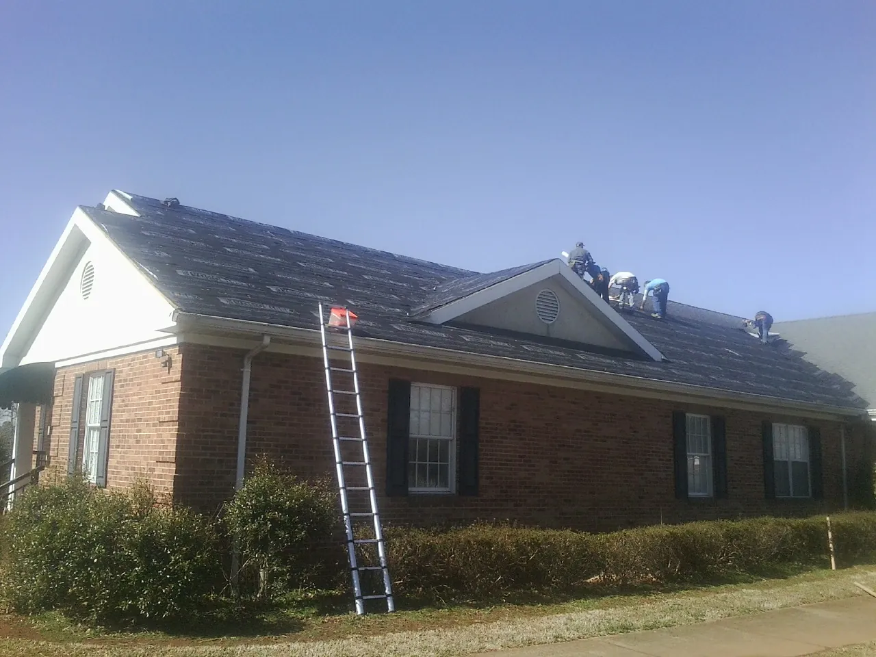 Crew tearing shingles off a brick ranch roof with a ladder set — Emergency Roof Repair work by our crew in Ellijay