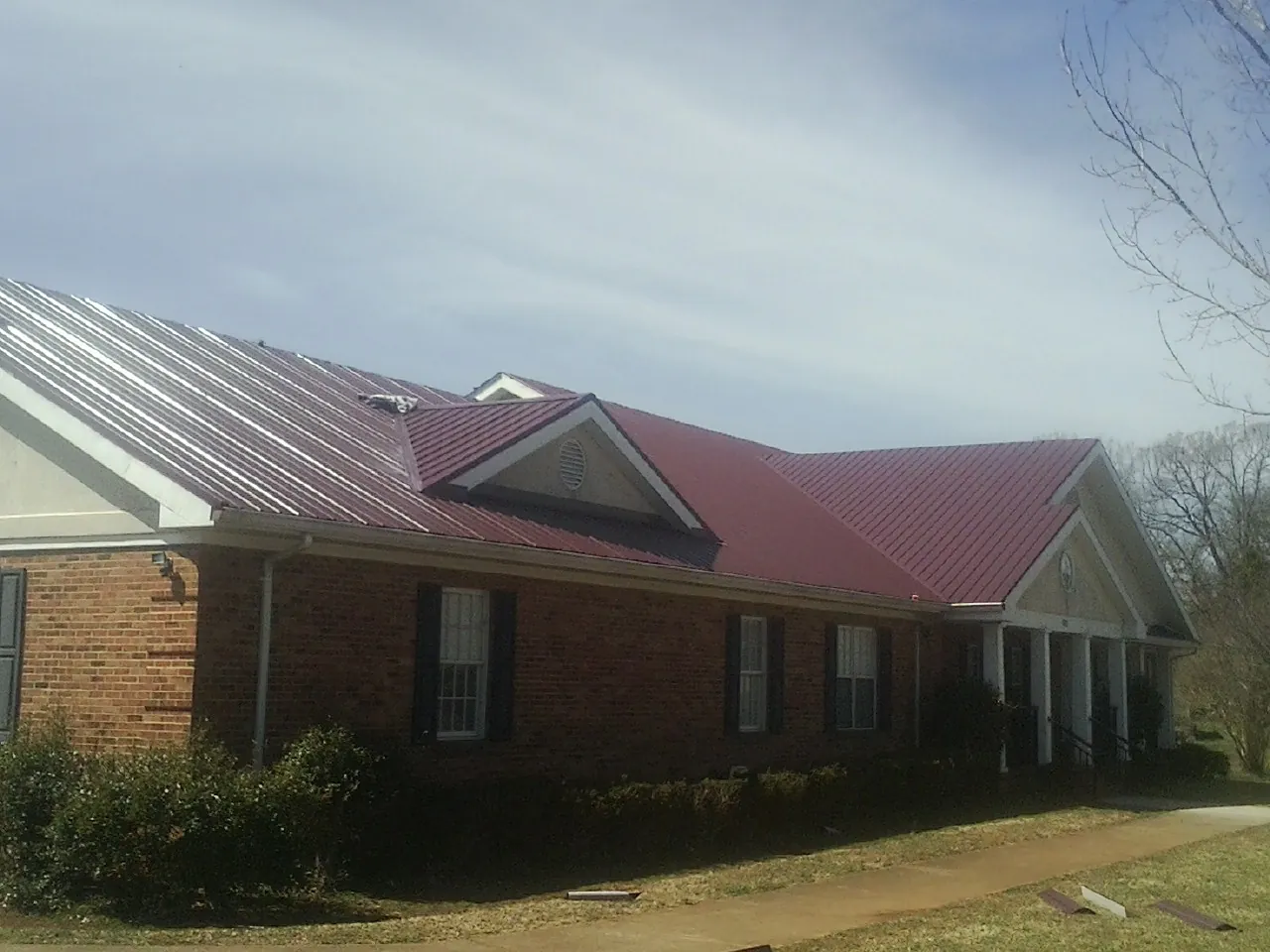 Red metal roof with gabled entries on a long brick building, from a Hail Damage Roof Repair job in Ellijay