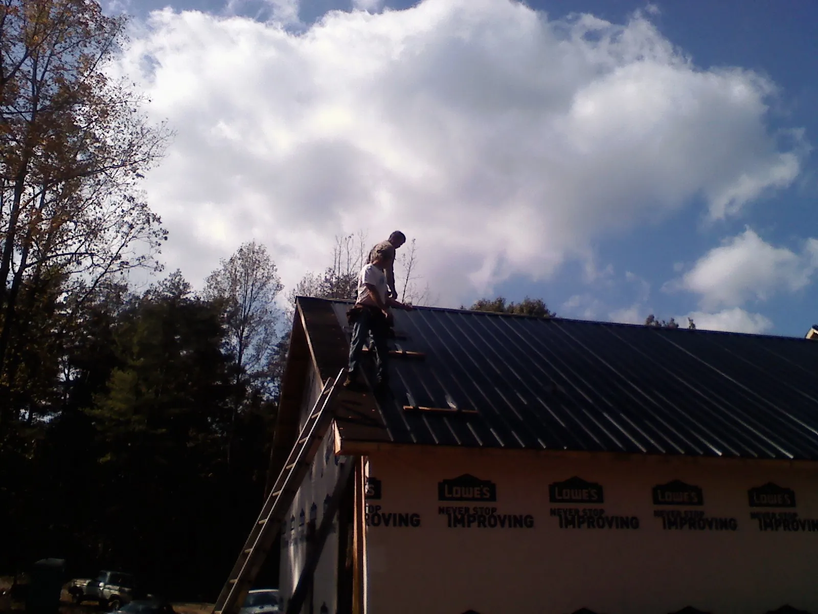 Roofer fastening dark metal panels high against a cloudy sky, from a Roof Inspection job in Ellijay