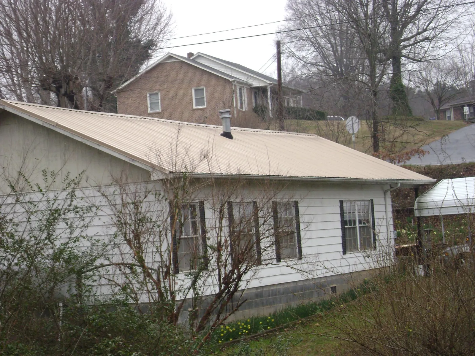 Tan metal roof on a white sided house set into a hillside — Commercial Roofing by Roofing Brothers in Ellijay